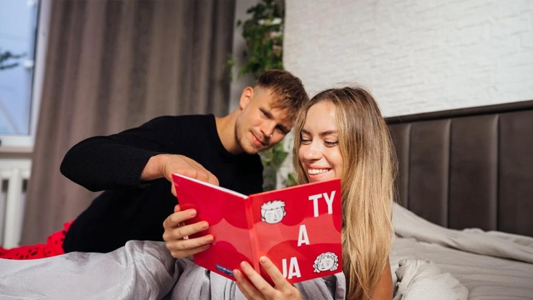Personalizovaná kniha Love Note ako romantický darček pre partnera, pár si číta červenú knihu v posteli.